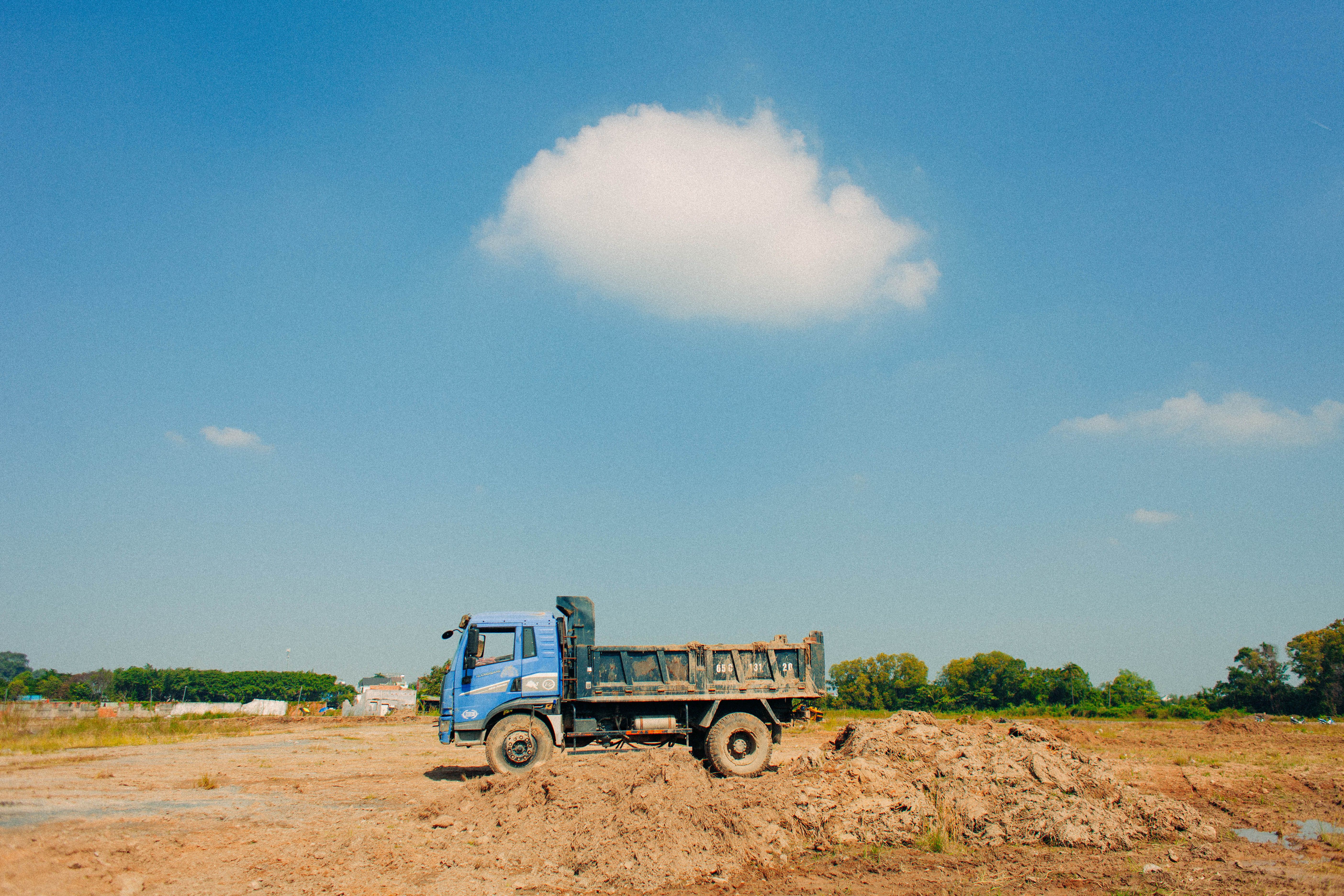 A blue dump truck parked on an open construction site under a clear blue sky with a single white cloud.