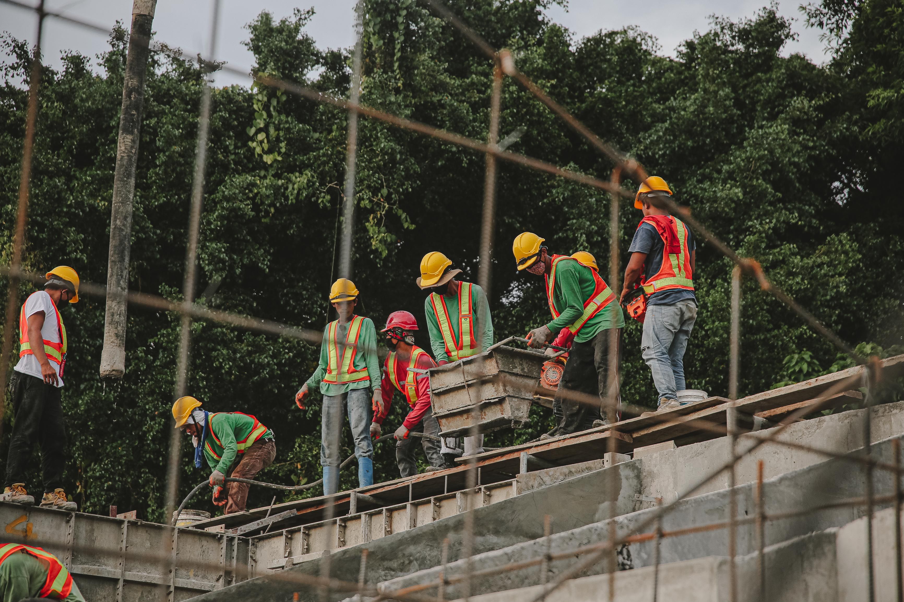 A group of construction workers in hard hats and safety vests working together on a building site with trees in the background.