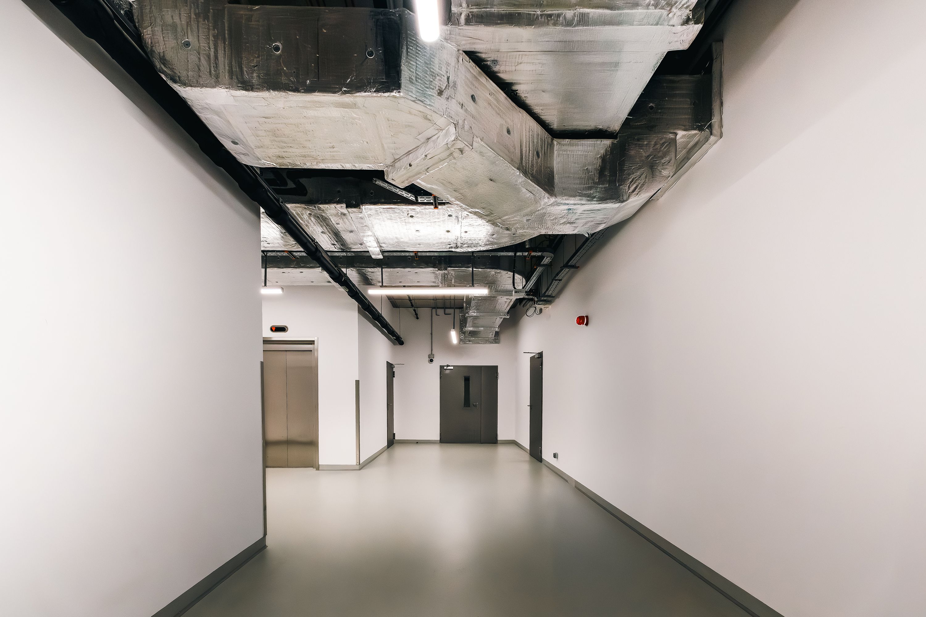 An empty commercial hallway under construction with white walls, a polished gray floor, and an exposed concrete ceiling.