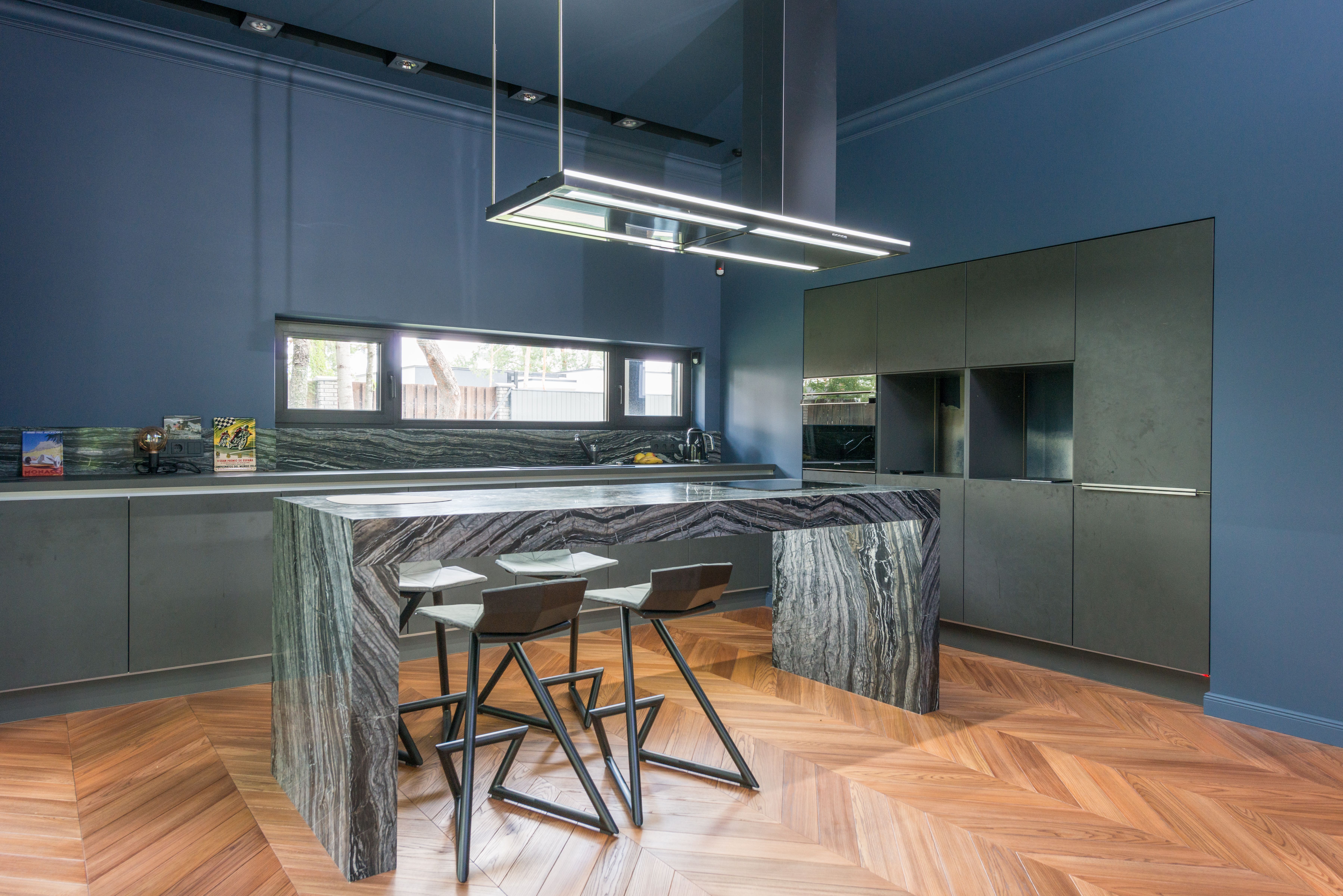A modern luxury kitchen with deep navy walls, dark gray cabinets, a dramatic veined green-stone island, and pendant lighting.