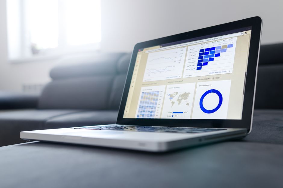 A laptop on a desk displaying an analytics dashboard with line charts, a heatmap, a world map, and a donut chart.