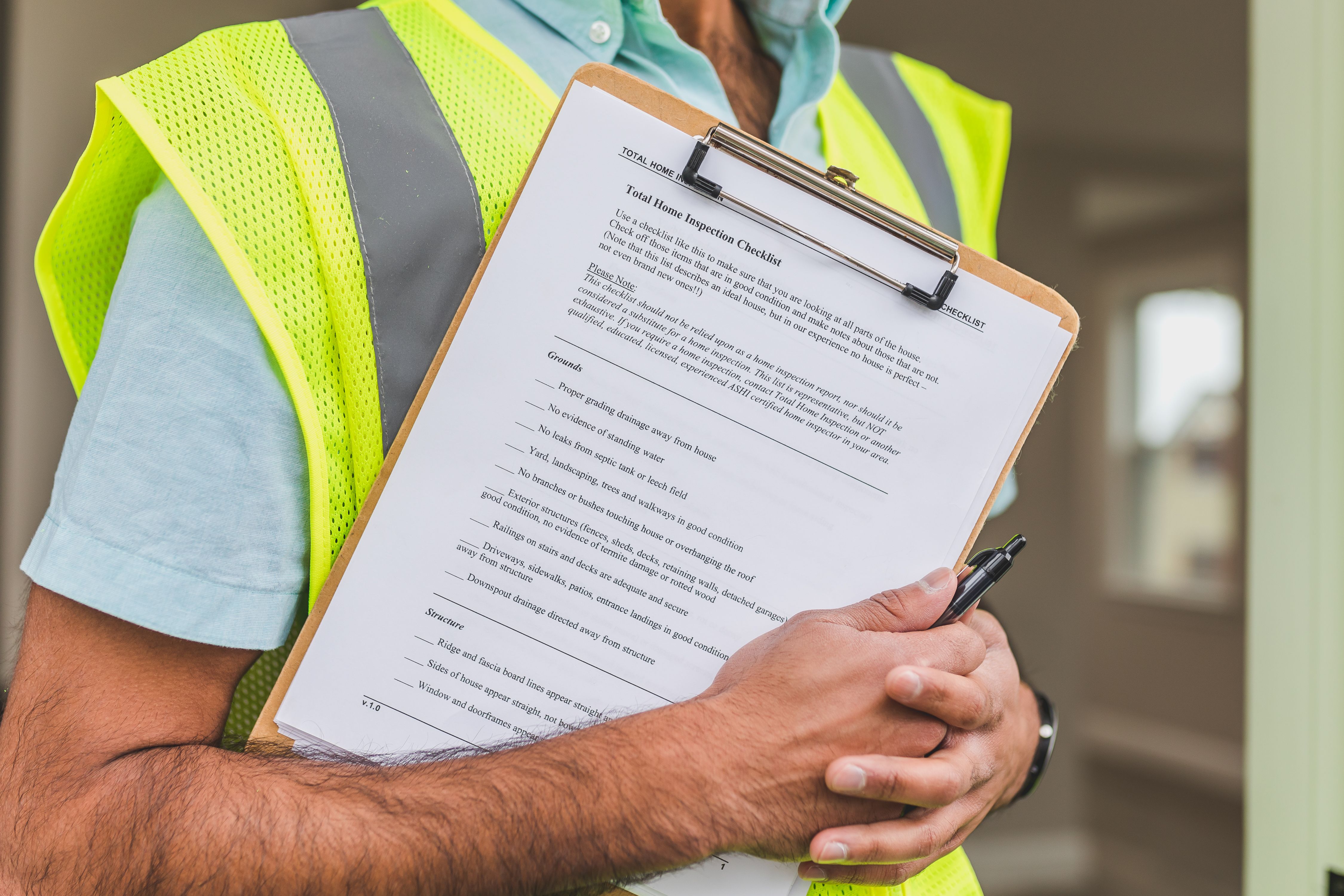 A close-up of a home inspection checklist on a clipboard held by an inspector in a high-visibility safety vest.