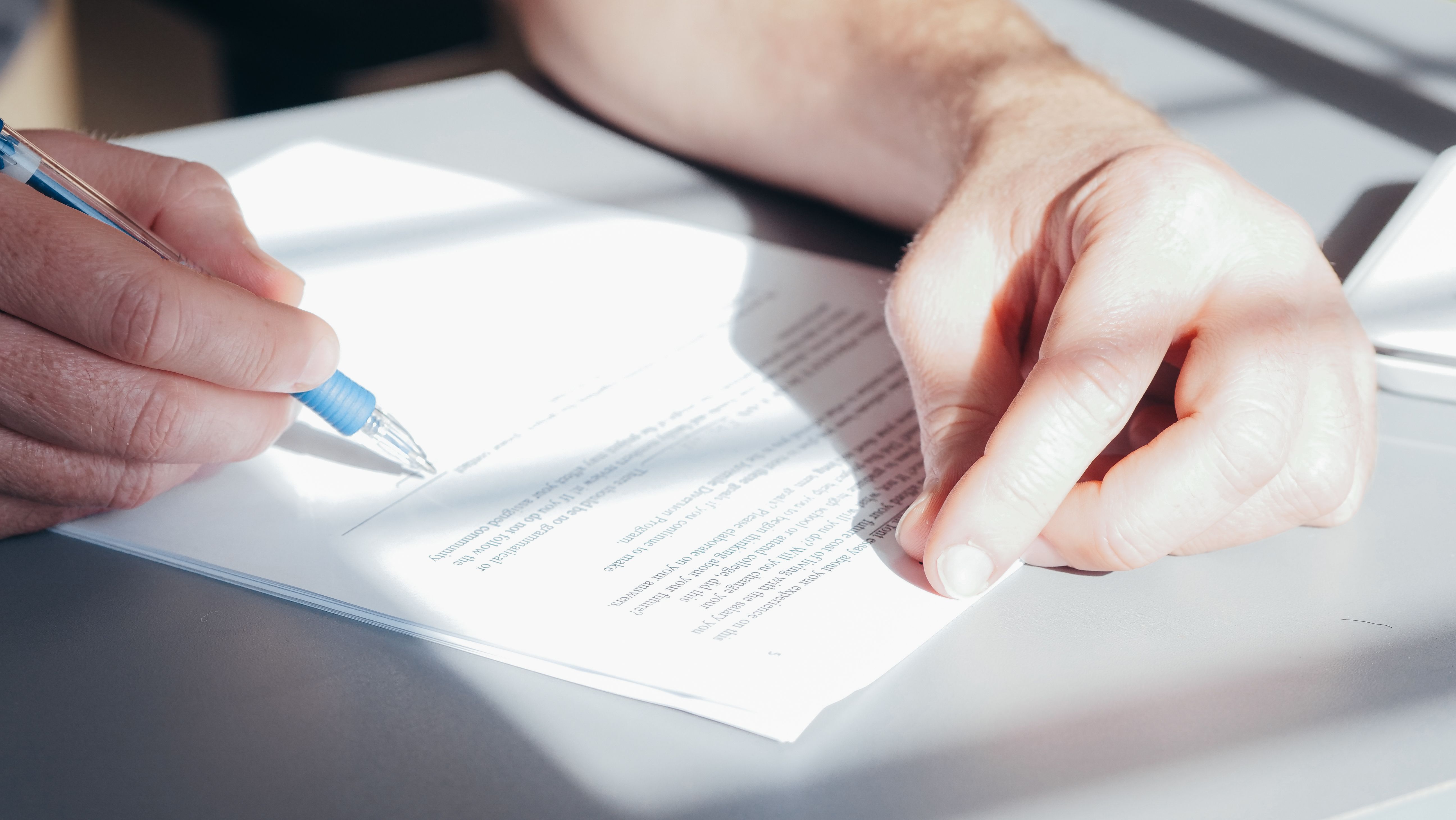 A close-up of hands reviewing a printed contract with a pen, ready to sign.