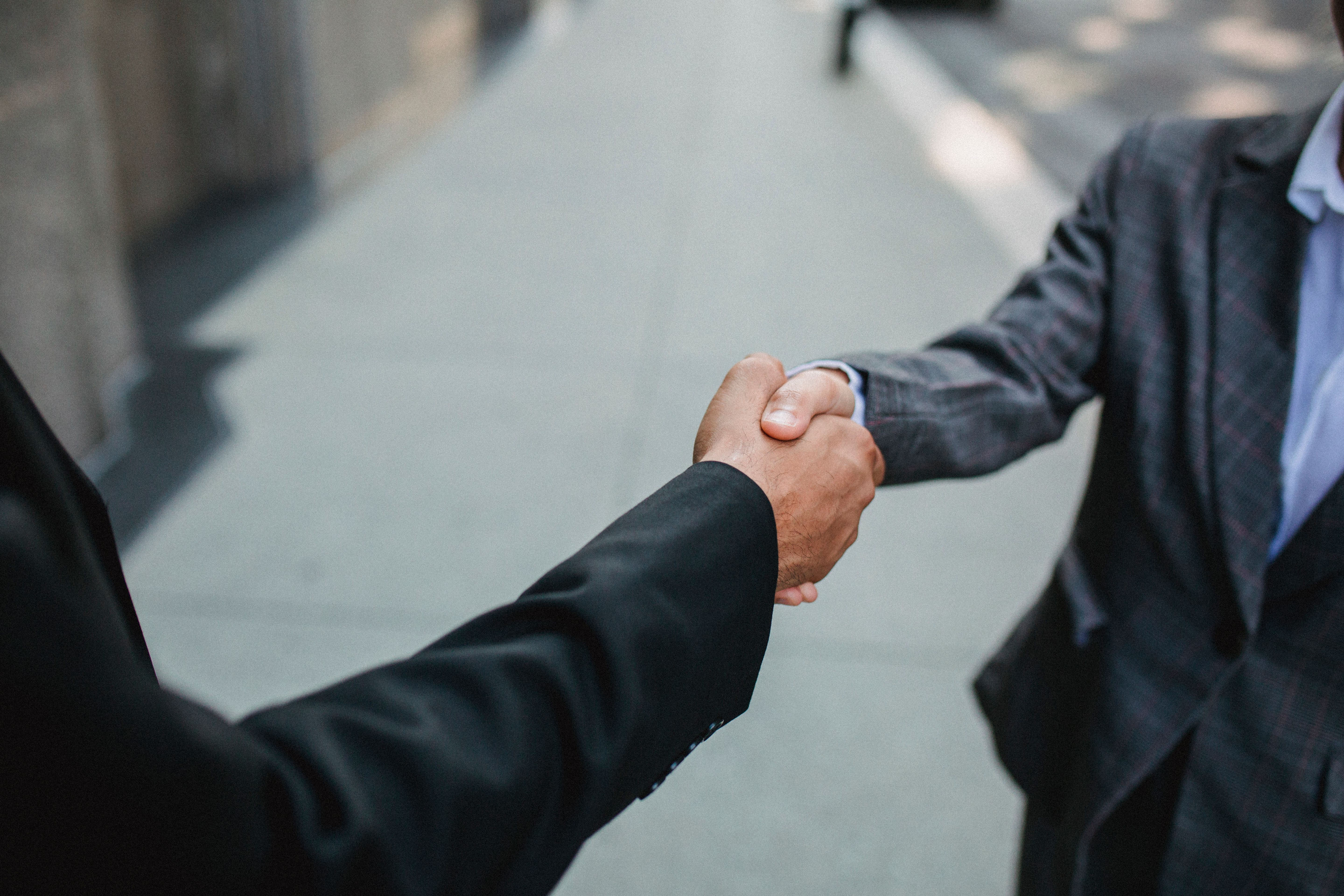 A close-up of two professionals shaking hands outdoors, symbolizing a tenant placement agreement.