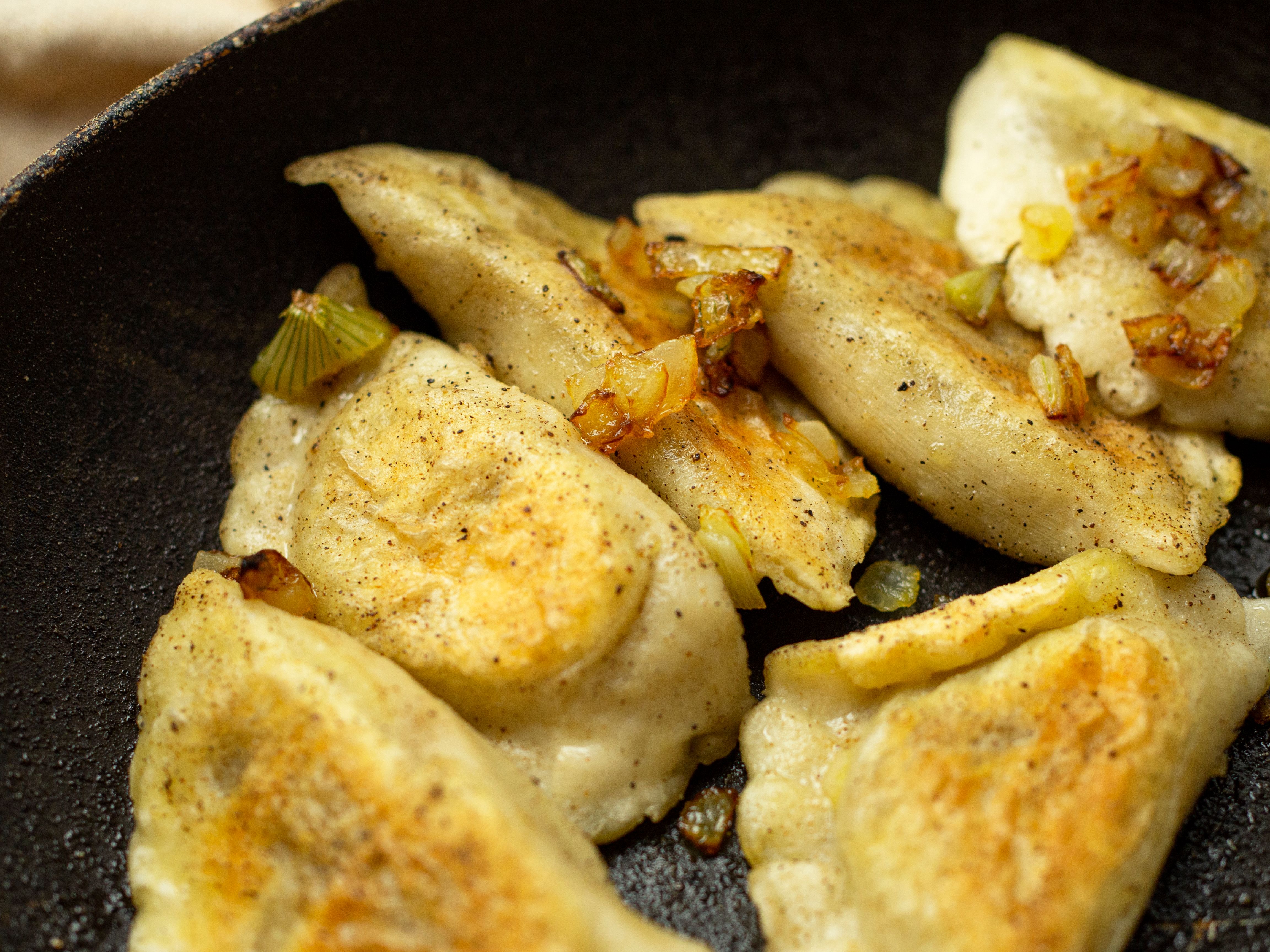 Golden pan-fried pierogi with caramelized onions in a cast-iron skillet at The Steel Hearth.