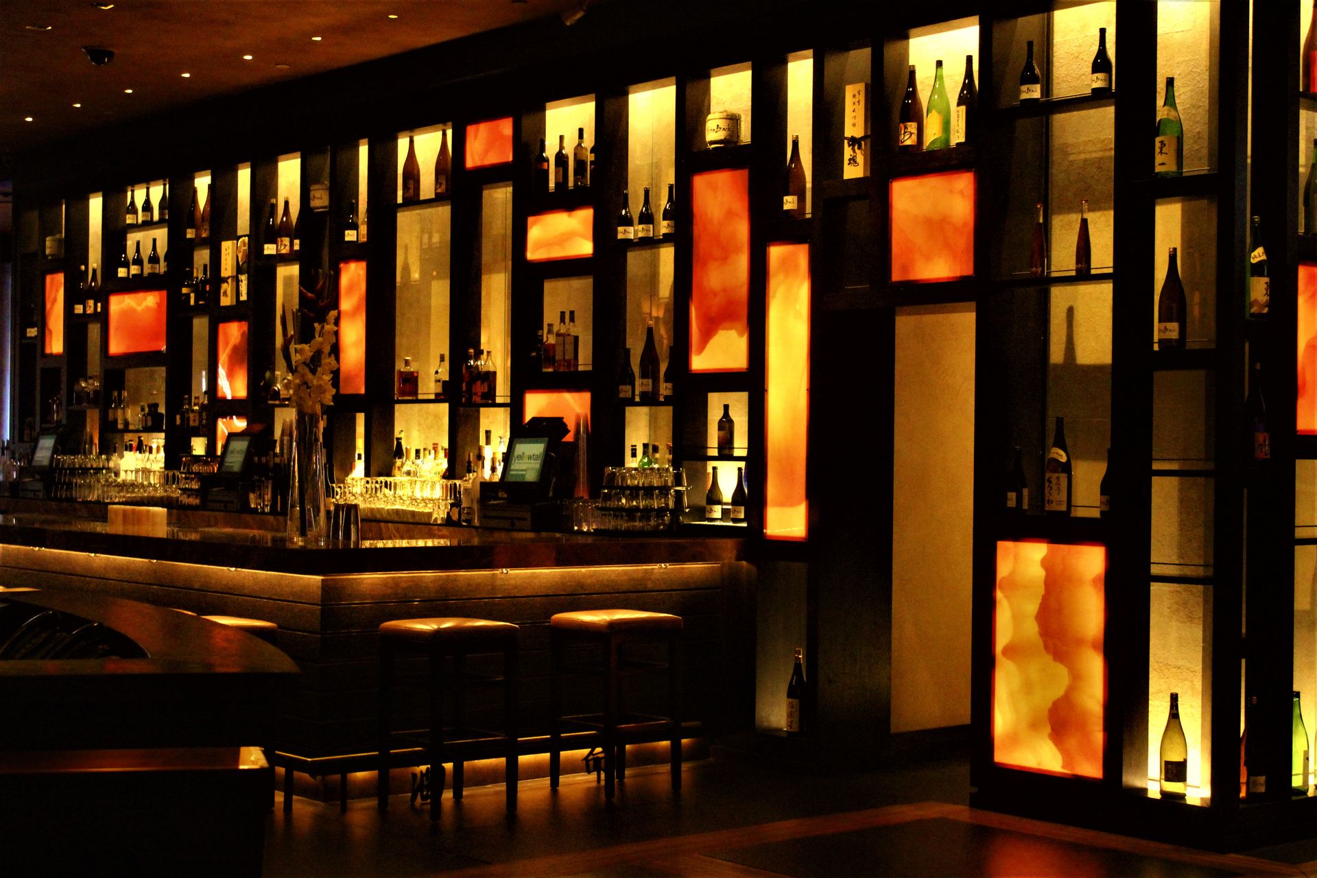 The backlit amber bar at The Steel Hearth, with glowing bottle cubbies and a long wood counter.