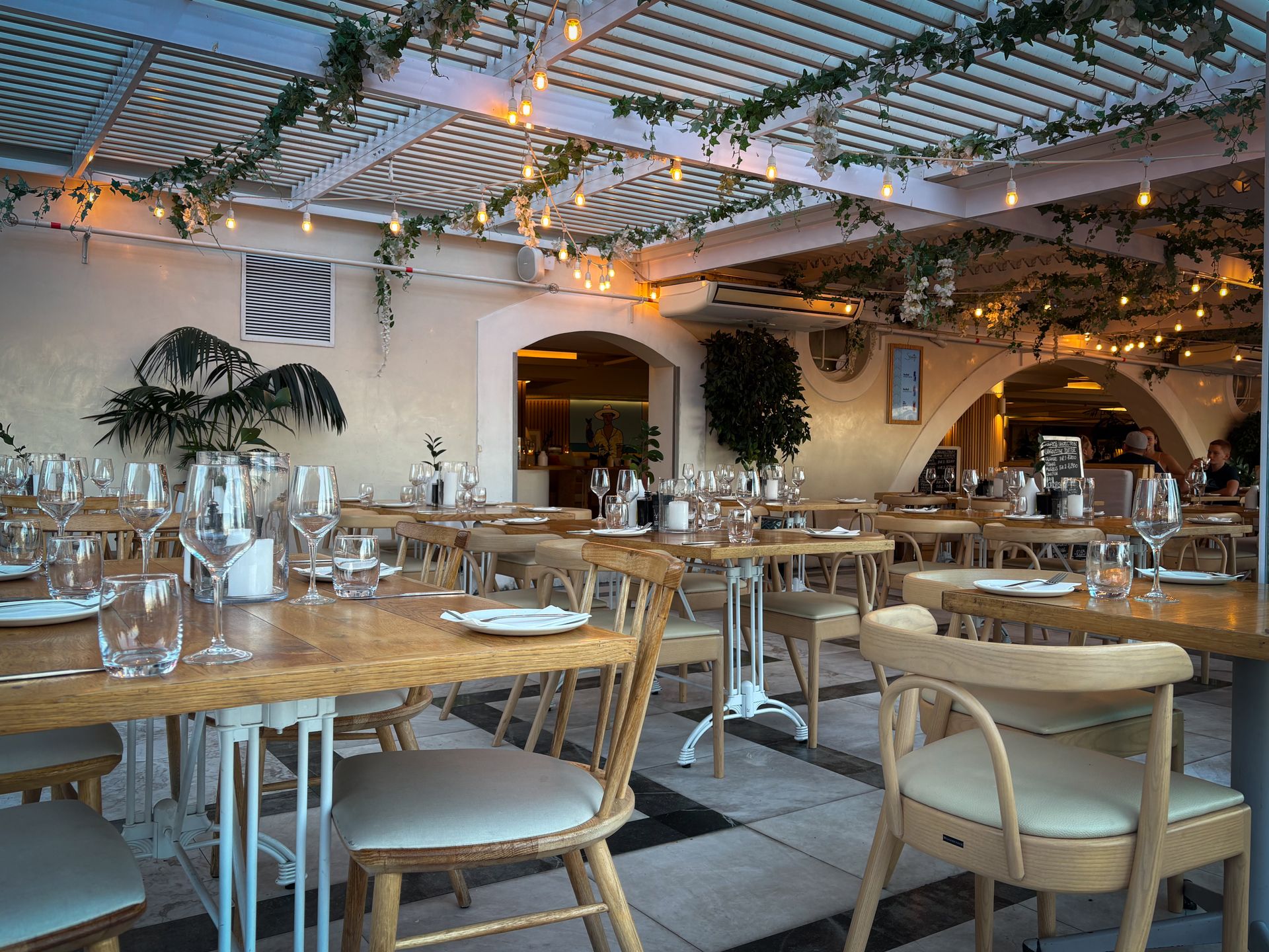 Warmly lit dining room with wooden tables, wine glasses, and string lights under a trellis ceiling at The Steel Hearth.