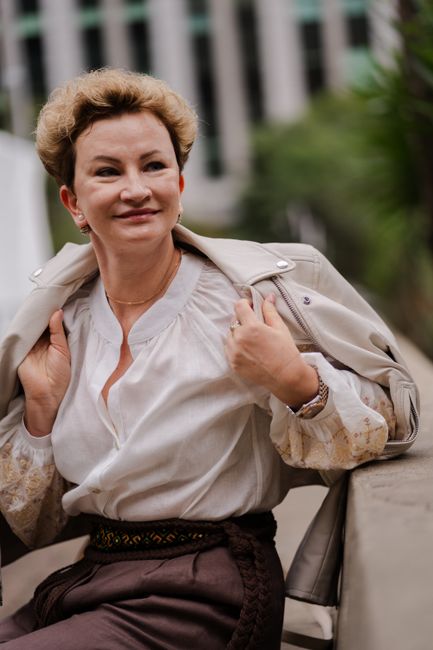 Angela Perri, owner and founder of Steel City Travel, a stylish woman in her 50s wearing a tan leather jacket over a white blouse, smiling warmly outdoors.