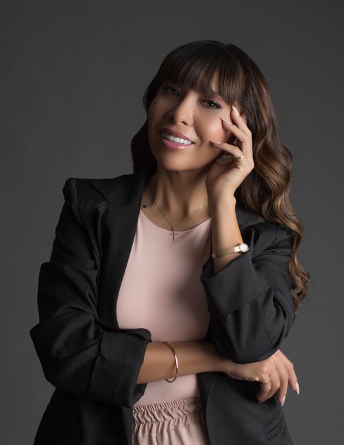 Maria Castellano, Senior Travel Advisor at Steel City Travel, a confident Latina woman in her 40s wearing a black blazer over a pink top, smiling warmly against a dark studio background.